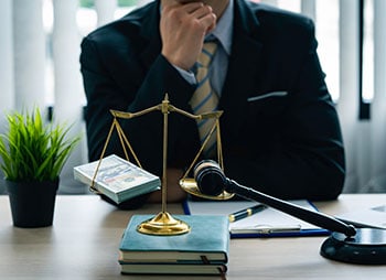 A man in a suit sitting at a desk with a scale of justice - Sharks at Law