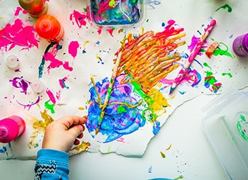 A child's hands covered in paint and holding paint brushes - Sharks at Law