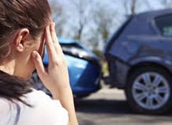 A woman holds her head in front of a damaged car - Sharks at Law