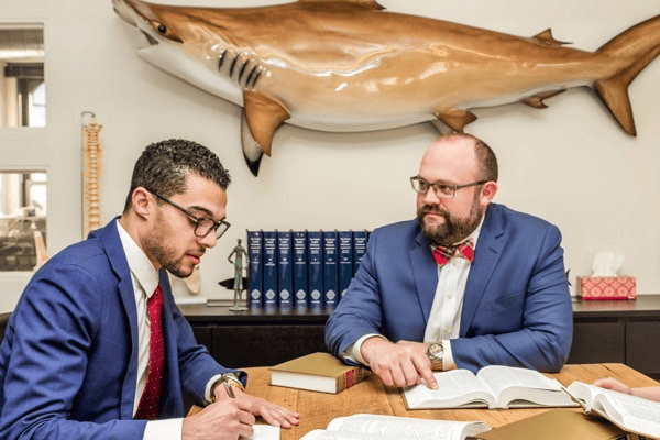 Two attorneys in suits sitting at a table - Sharks At Law